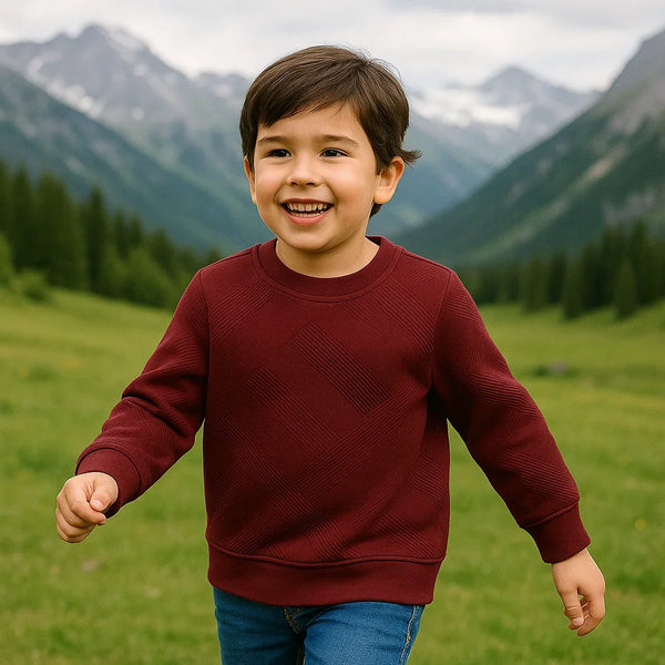 Smiling boy wearing maroon sweatshirt and blue jeans in green mountain valley outdoors