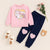Baby pink unicorn print sweatshirt with navy pants featuring pink heart patches, white shoes, and flowers