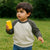 Toddler in grey and off-white raglan sweatshirt holding yellow toy outdoors on grass