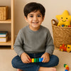 Smiling boy in light grey textured sweatshirt and jeans sitting on carpet with colorful toy blocks