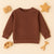 Textured brown toddler sweatshirt on beige background with wooden toys camera star car and rake